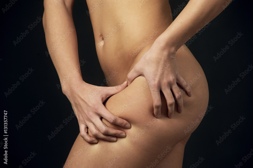 Naklejka premium Woman pinches her thigh to control cellulite , on a dark background