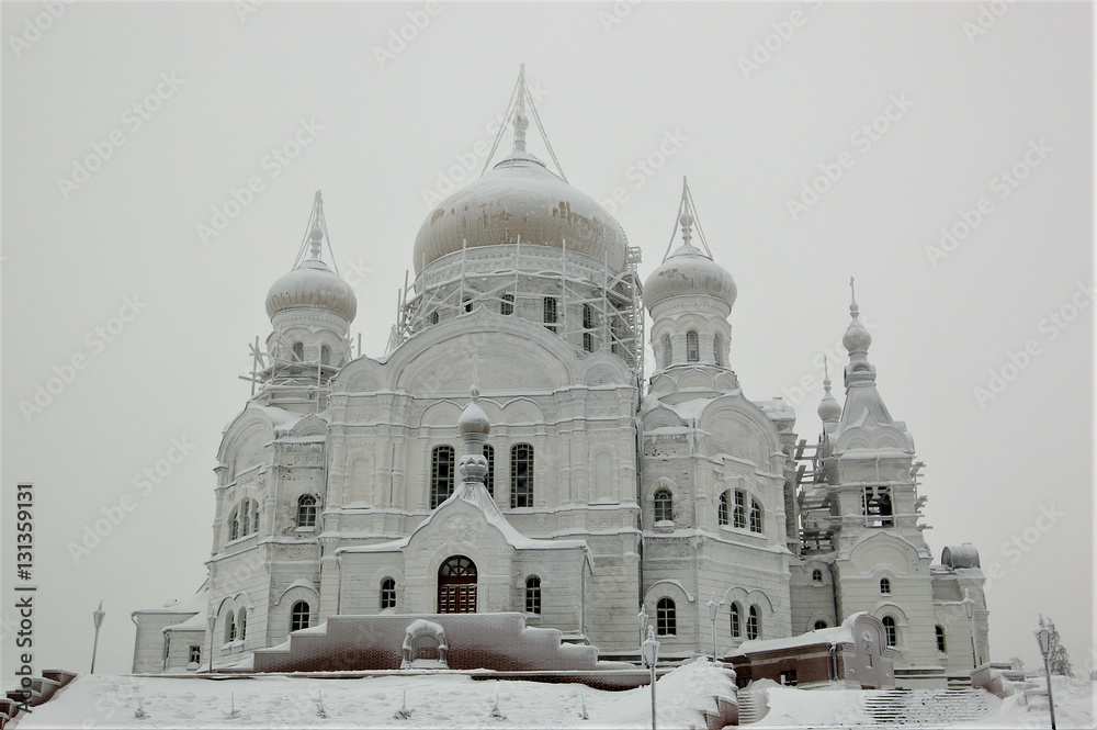 Obraz premium Белого́рский Свято-Никола́евский православно-миссионе́рский мужско́й монасты́рь. Крестовоздвиженский собор в снежном инее на высокой горе и заснеженная дорога к нему. Зима
