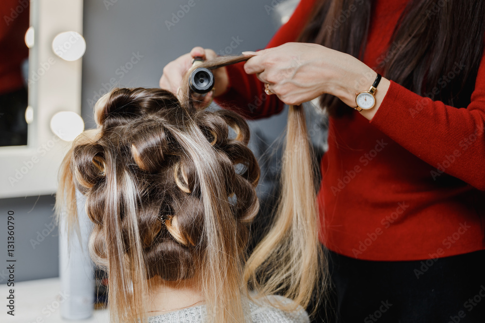 stylist making ringlets to brunette woman. Hairdresser working w