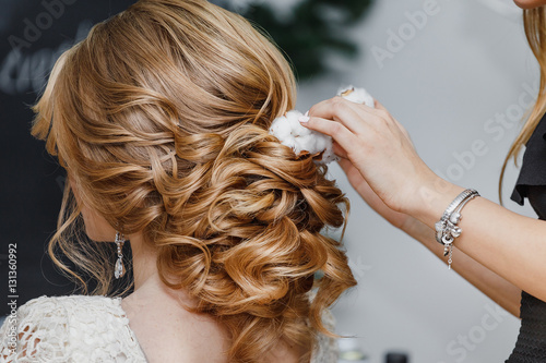 Hair stylist or florist makes the bride a wedding hairstyle with