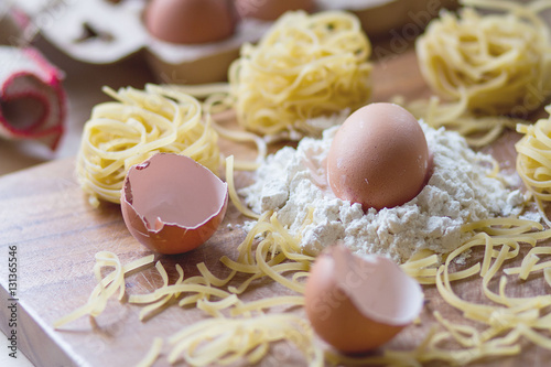 An egg on top of white flour with Chinese noodles, egg shell on chopping board and eggs in box in background, a preparation for cooking, Italian spaghetti,mie, typical Chinese food 