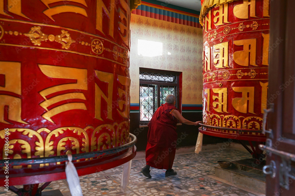 Old bouddhist monk, a tibetan man, spins a huge prayer wheels at the Shechen monastery, Kathmandu, Nepal.