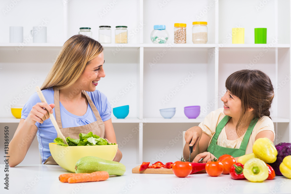 Happy mother and her daughter enjoy making healthy meal together at their home.