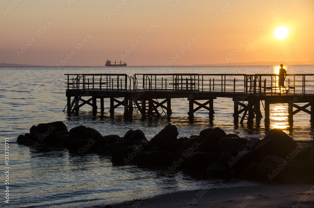 Man on the jetty going for a swim in the wild in the sunrise
