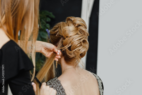 Hairdresser makes upper bun wedding hairstyle close-up on sandy blond hair of beautiful woman
