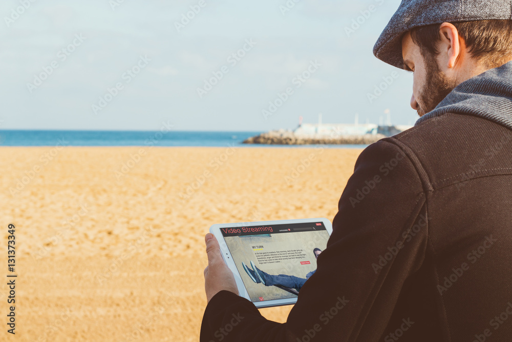 Video streaming concept. Man relaxing with digital tablet outdoor on the beach.