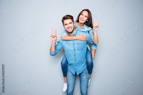 Smiling happy man piggybacking his girlfriend and gesturing v-si