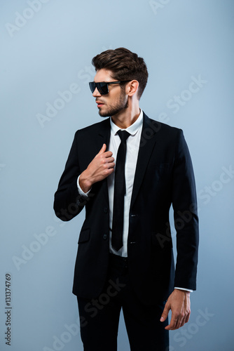 Young stylish businessman in black glasses touching suit