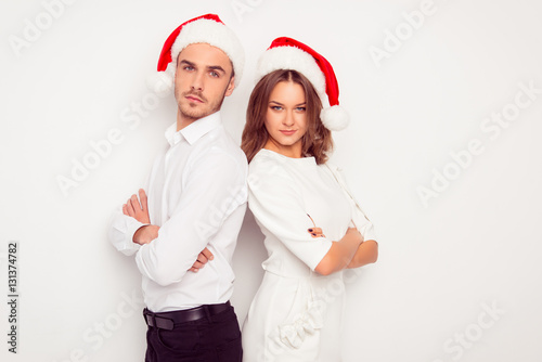 Two confident serious man and woman in santa hats standing back