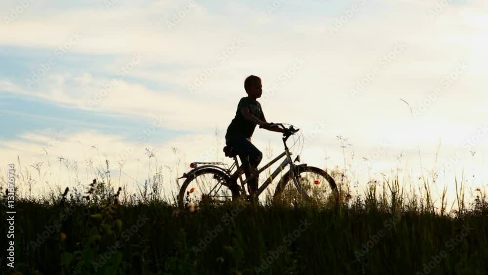 Little kid riding bike in summer meadow landscape at beautiful sunset sky background. Silhouette of anonymous caucasian small boy of 9 years old sitting on bicycle in countryside area. Real time video Little kid riding bike in summer meadow landscape at beautiful sunset sky background. Silhouette of anonymous caucasian small boy of 9 years old sitting on bicycle in countryside area. Real time video