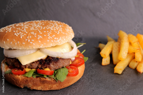 Homemade cheeseburger with arugula, mini tomatoes and homemade French fries on the stone slate board.