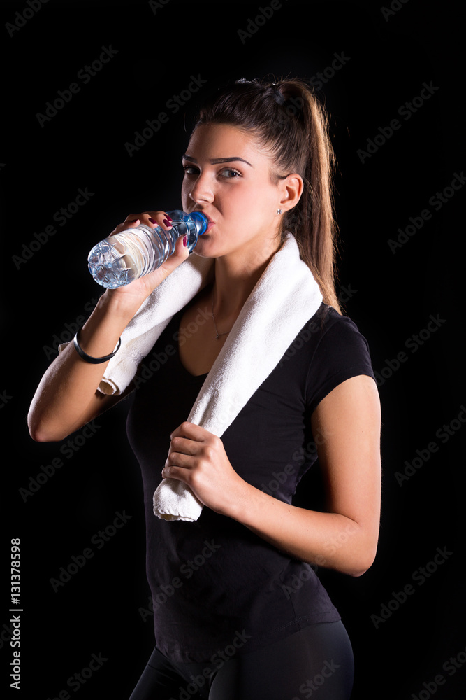 young fitness girl with towel drinking water from plastic bottle young fitness girl with towel drinking water from plastic bottle