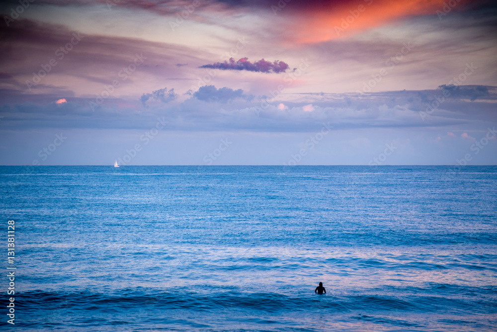 Surfer and the yacht with sail in the open Sea at the sunset.
