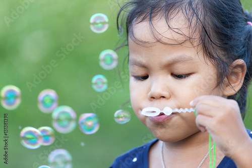 Cute asian little girl is blowing soap bubbles