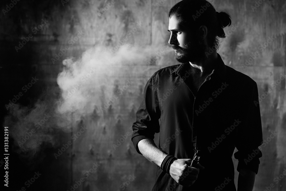 young bearded gothic hipster man smokes electronic cigarette. a man dressed  in black Stock Photo | Adobe Stock
