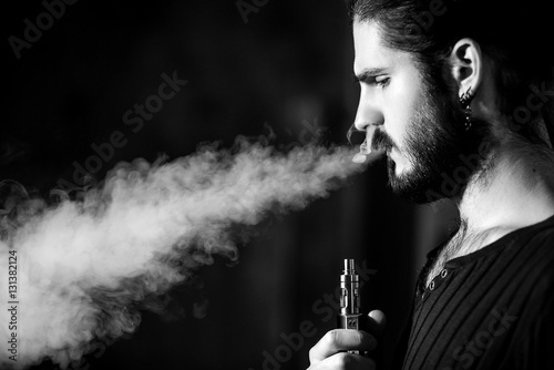 young bearded hipster man smokes electronic cigarette. 