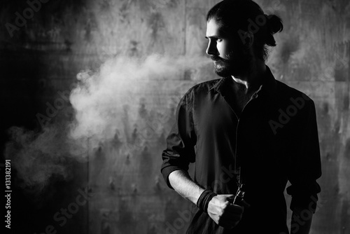 young bearded gothic hipster man smokes electronic cigarette. a man dressed in black
