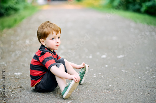 Little boy sitting on the ground in the summer park