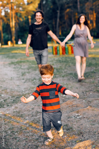 A little boy runs away from his parents in the summer in the park