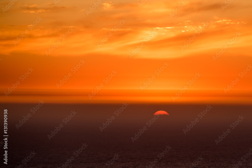 Vivid sunset in orange colors with sun disk hiding in Atlantic ocean