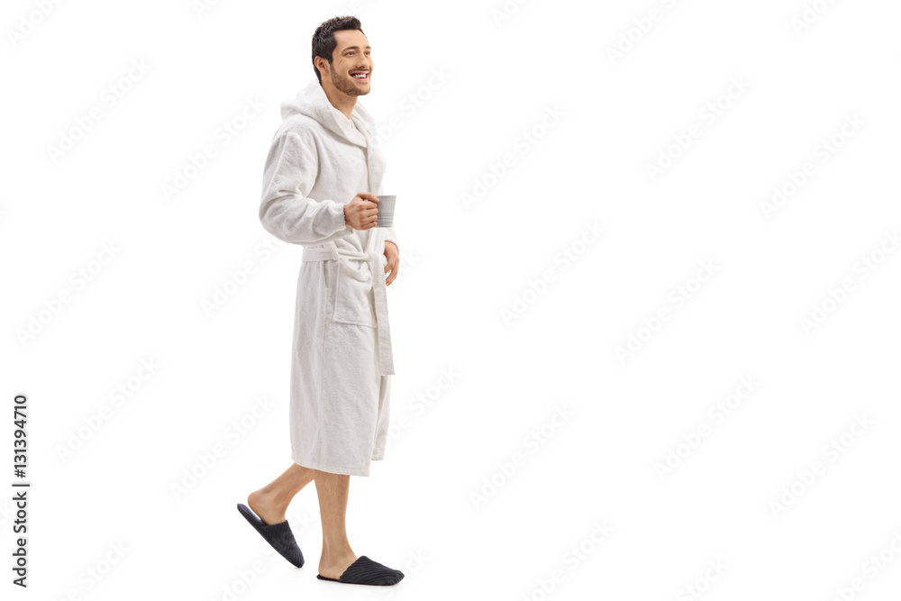 Young man in a bathrobe holding a cup and walking - obrazy, fototapety, plakaty 