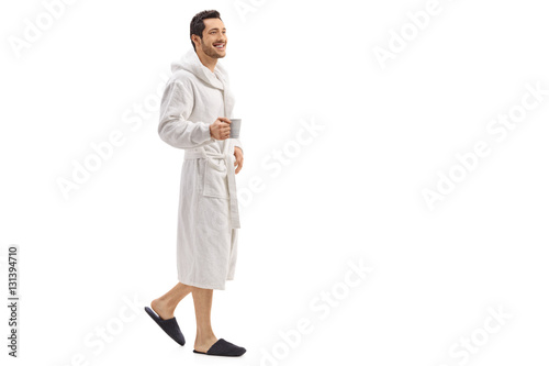 Young man in a bathrobe holding a cup and walking photo