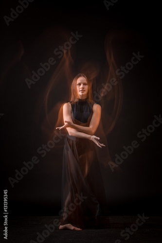 Young beautiful dancer in beige dress dancing on black background