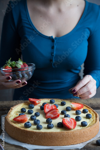 The girl is preparing a cheesecake with fresh berries