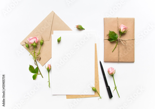 Letter, envelope and gift on white background. Invitation cards, or love letter with pink roses. Holiday concept, top view, flat lay
