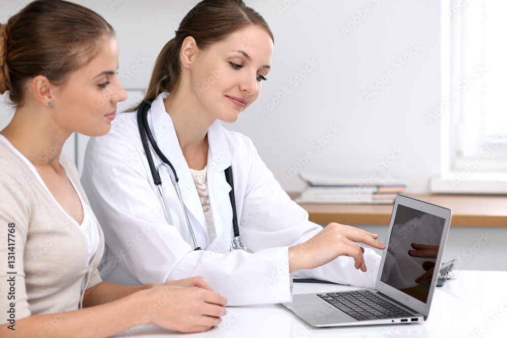 Doctor and patient sitting at the desk. Physician pointing into laptop computer. Medicine and health care concept Doctor and patient sitting at the desk. Physician pointing into laptop computer. Medicine and health care concept