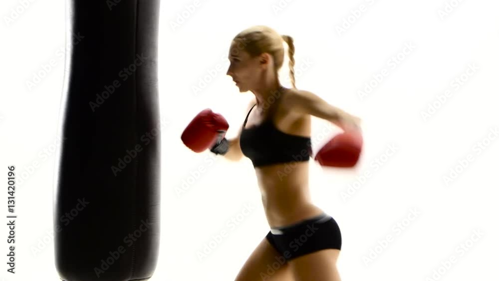 Kickboxer woman fulfills blows on punching bag. White studio Kickboxer woman fulfills blows on punching bag. White studio
