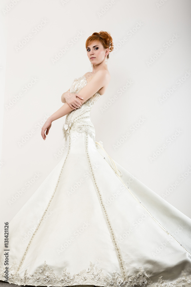 Fototapeta premium Beautiful young redhead bride wearing white wedding dress with professional make-up and hairstyle