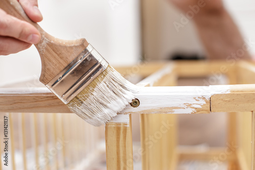 Fototapeta Naklejka Na Ścianę i Meble -  Man painting wood furniture with a brush and paints, close-up