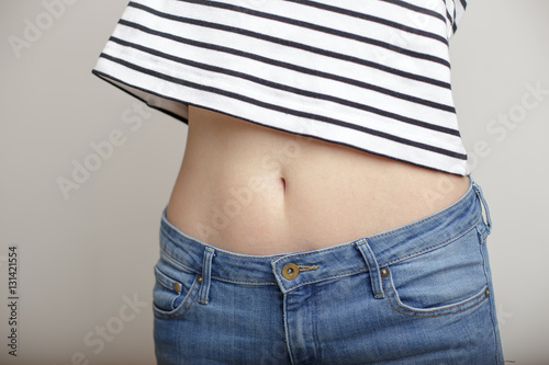 girl in blue jeans and a striped sweater and lifted her arms bared belly with a beautiful waist and umbilicus photo