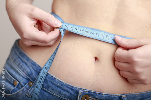 fair-skinned woman in blue jeans is measured using a tape beautiful slender waist photo