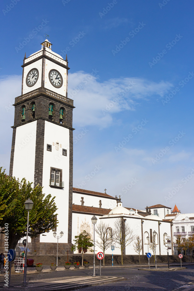 Fototapeta premium St. Sebastian Church tower with bells and clock in Ponta Delgada on Sao Miguel Island in Azores, Portugal. The Main Church of the city and surrounding buildings on a sunny winter day.