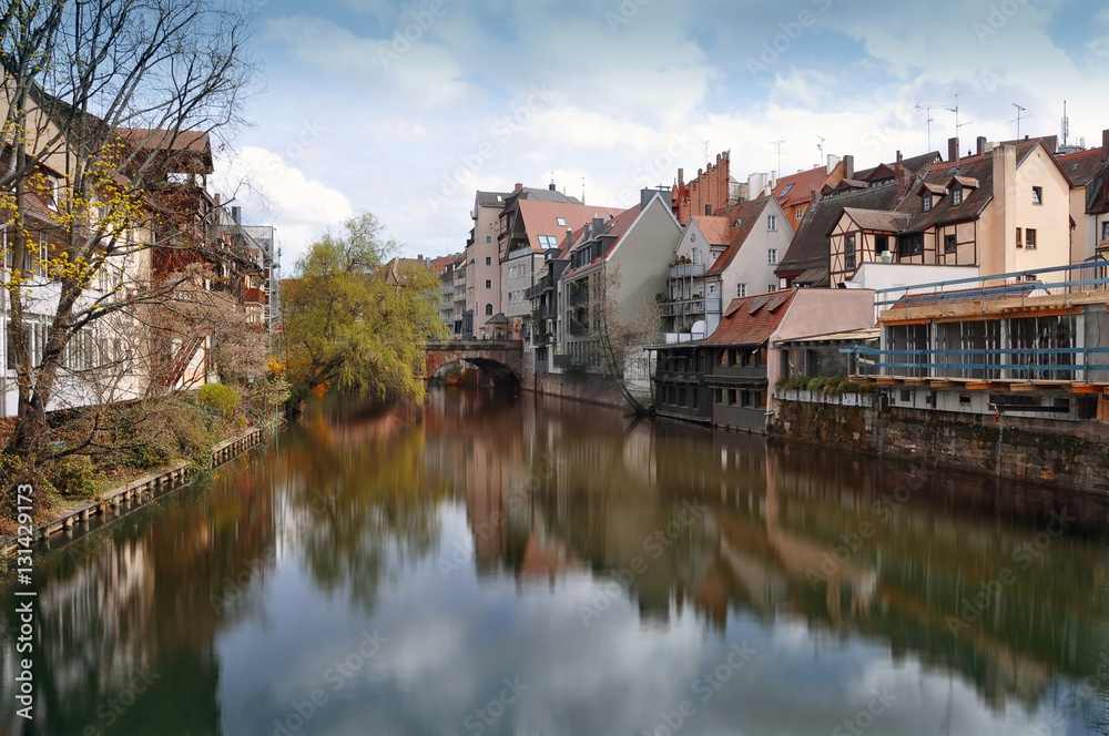 Old buildings, arch bridge and tree reflected in water. Nuremberg, Bayern, Germany