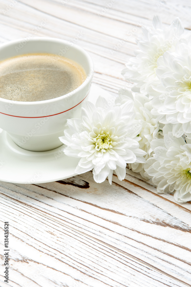 cup of coffee and flowers on light wooden table