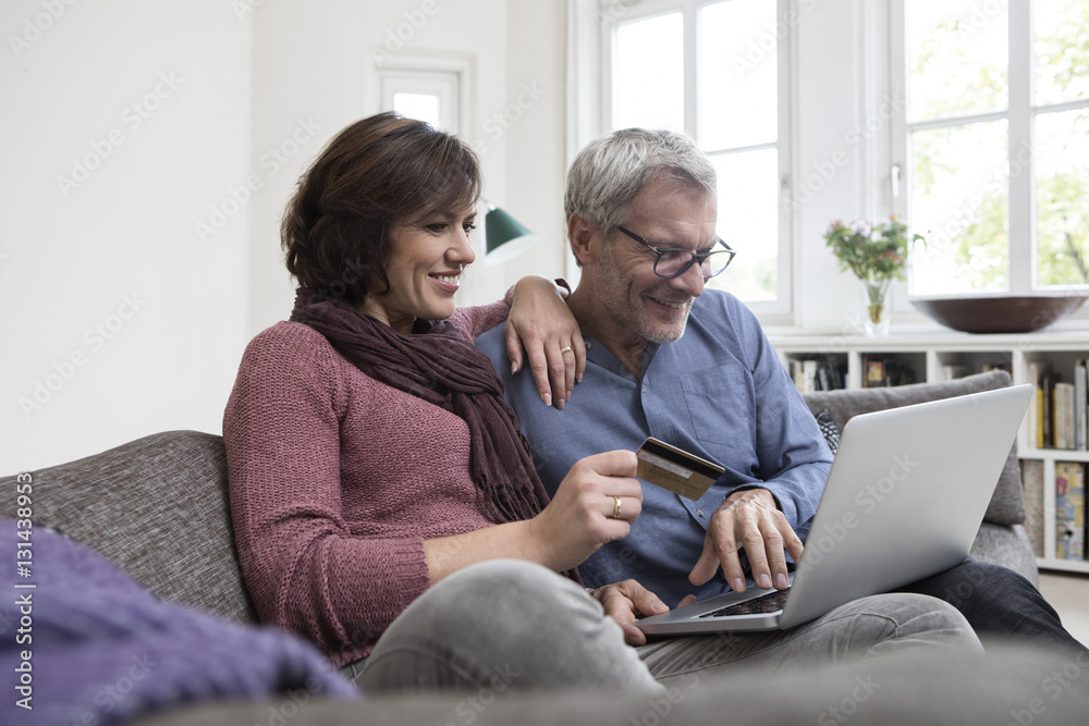 Smiling mature couple at home on the sofa shopping online Smiling mature couple at home on the sofa shopping online
