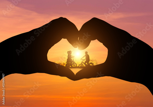  silhouette little boy and little girl having fun riding bike on sunset in the middle silhouette hands heart shape 