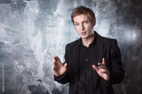 Photography young man conducts a dialogue in black suit on textured grey background