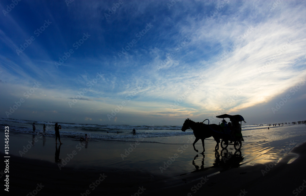 Silhouettes of horse with a cart and people relaxing at Parangtritis Beach famous by its black sands, Central Java, Indonesia. Silhouettes of horse with a cart and people relaxing at Parangtritis Beach famous by its black sands, Central Java, Indonesia.