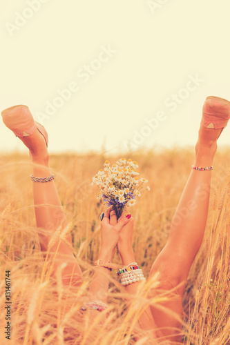 Girl s legs with flowers in the wheat field.  