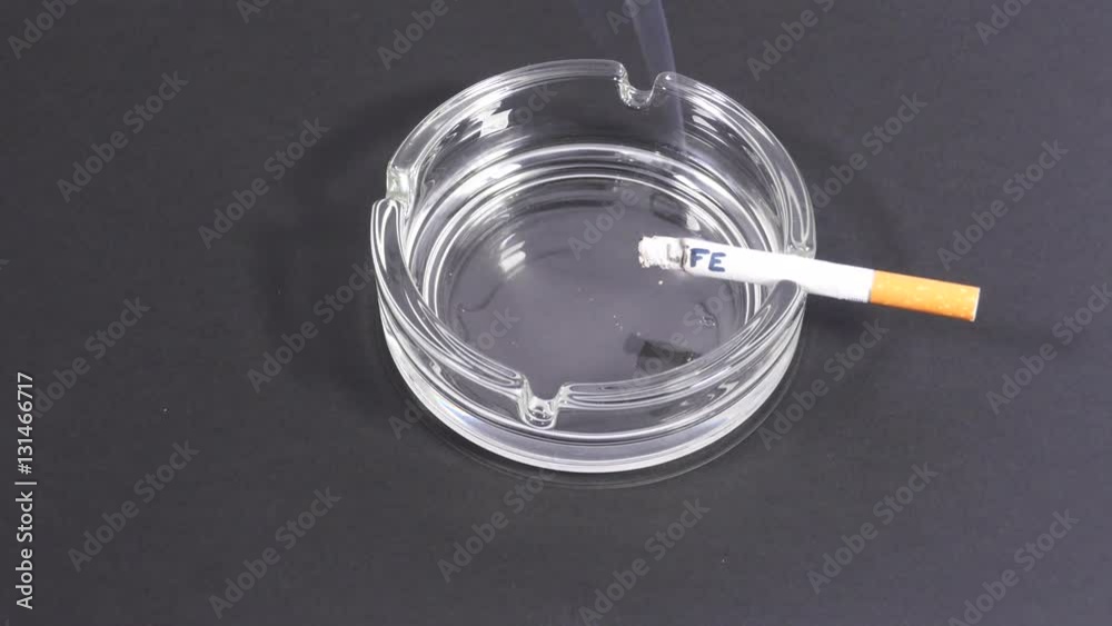 Burning inscription on cigarette. Cigarette with the written word 'life' smoldering in a transparent ashtray. Burning inscription on cigarette. Cigarette with the written word 'life' smoldering in a transparent ashtray.
