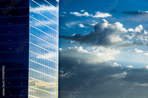 modern office building exterior with glass windows reflecting sky and clouds
