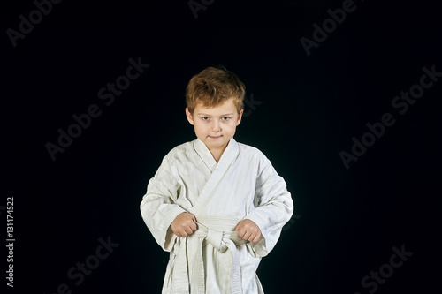 Young boy in kimono shows the martial arts on a black background