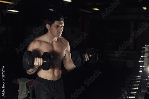 Muscular man working out in gym doing exercises with dumbbells at biceps, strong male naked torso abs.