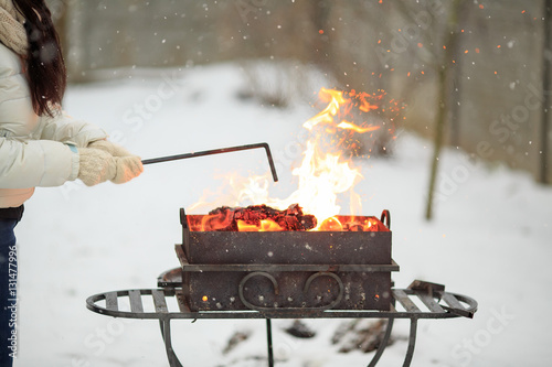 Hand with poker adjusts the coals in the brazier. Lighting the barbecue in the backyard in the winter.