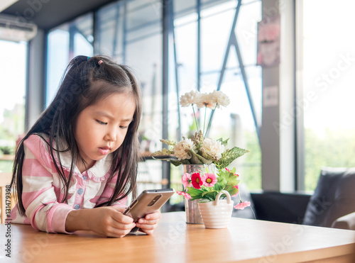 Portrait of Asia pretty little girl play mobile phone, serious f © bjginny