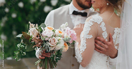 Fotografiet stylish bride and groom are holding bridal bouquet